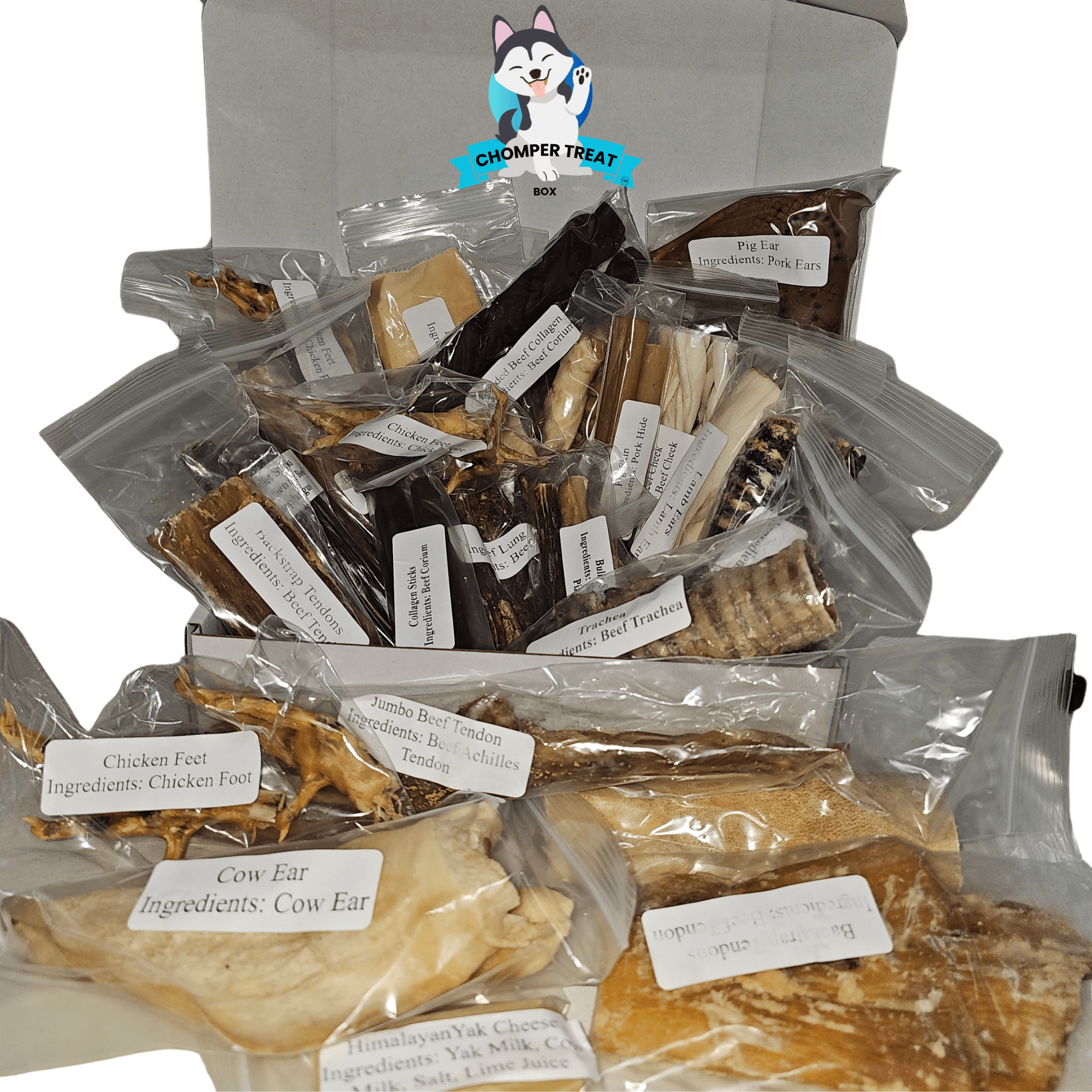 Deluxe Chomper Treat Box with various all-natural dog chews, including cow ears and chicken feet, in clear packaging.