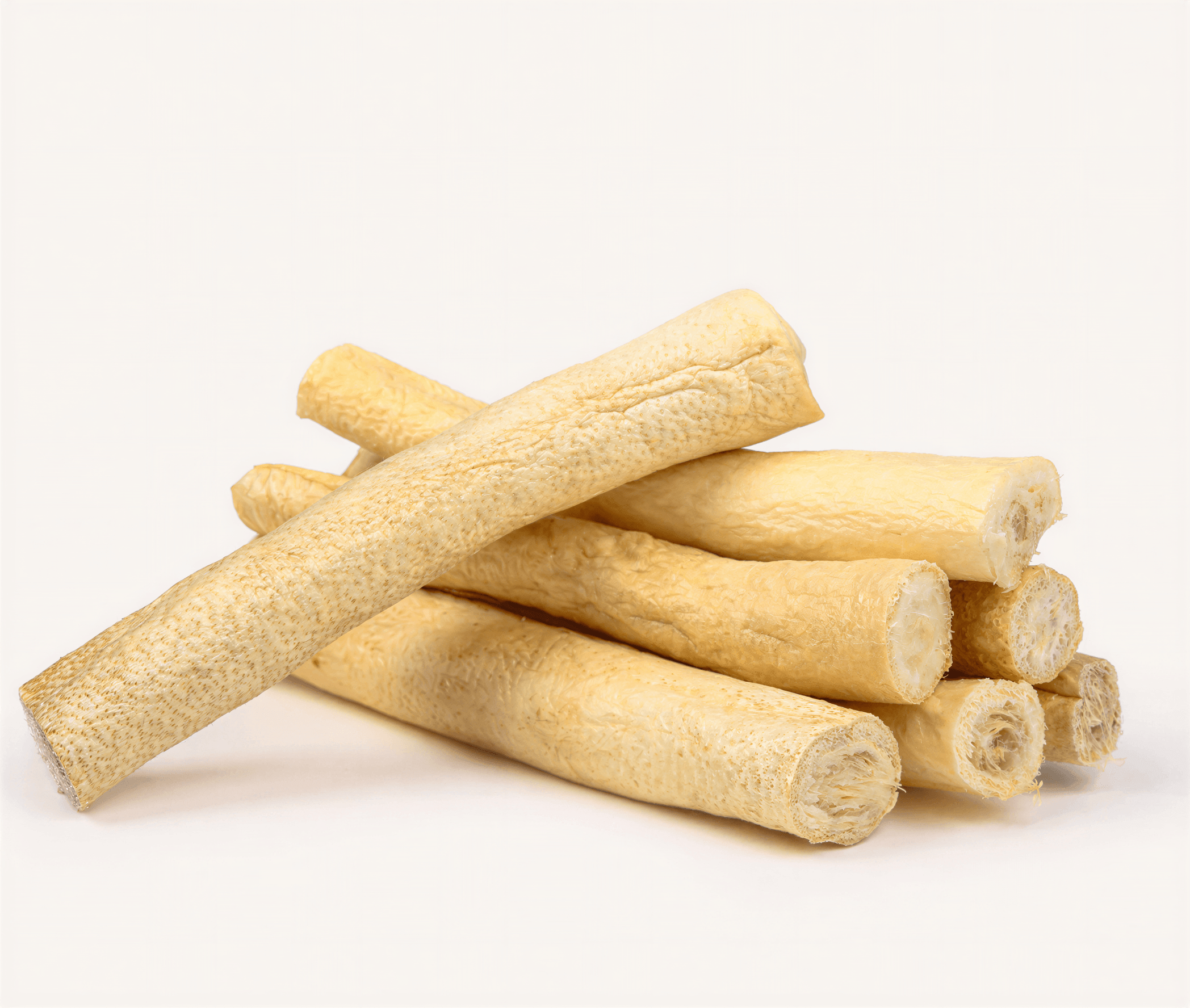 Cow Tails all natural dog chews stacked on a light background, showcasing their elongated, beige shape.