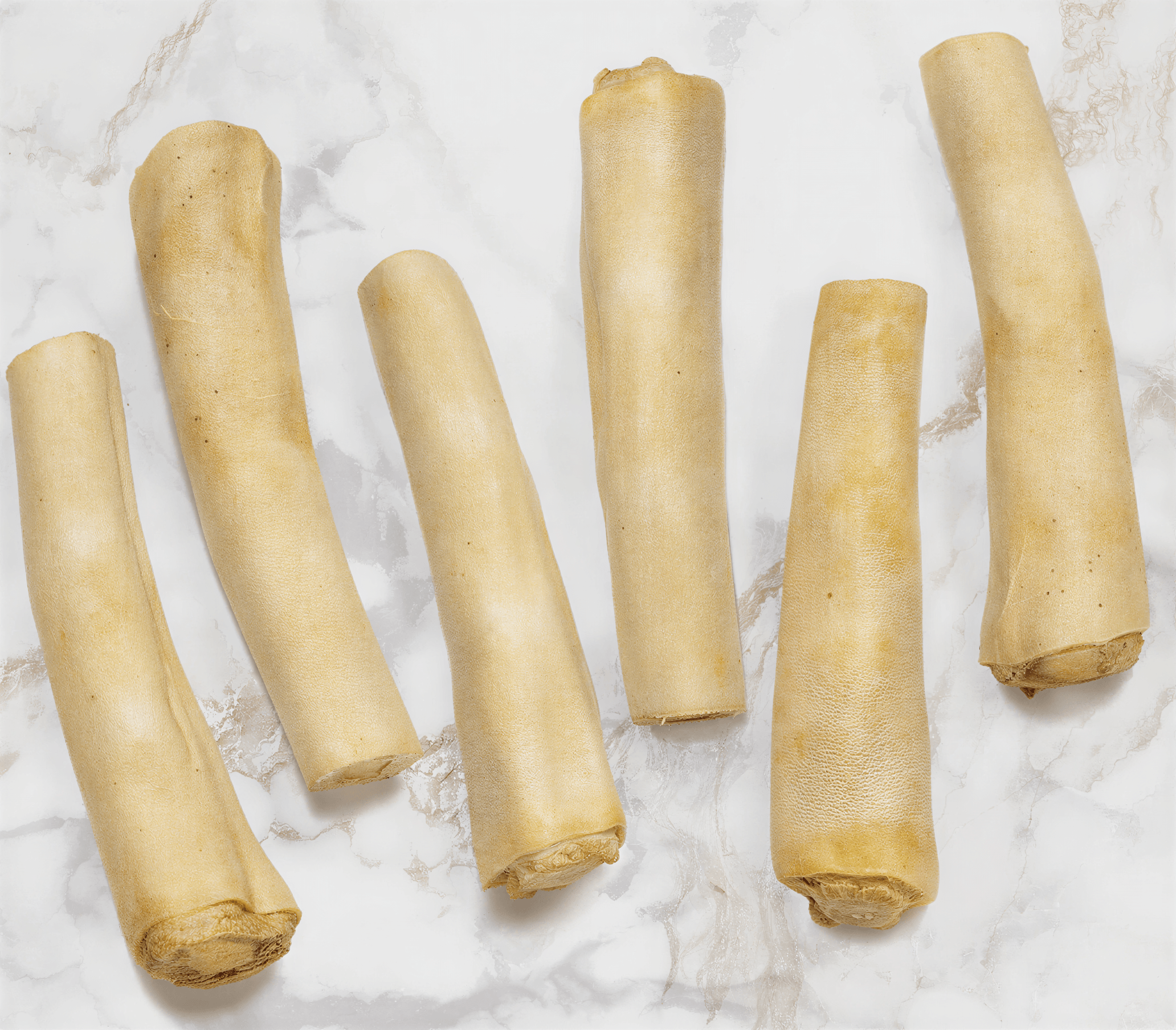 Cow Tails all natural dog chews in an 8 pack, featuring six light brown, elongated hard chews on a marble background.