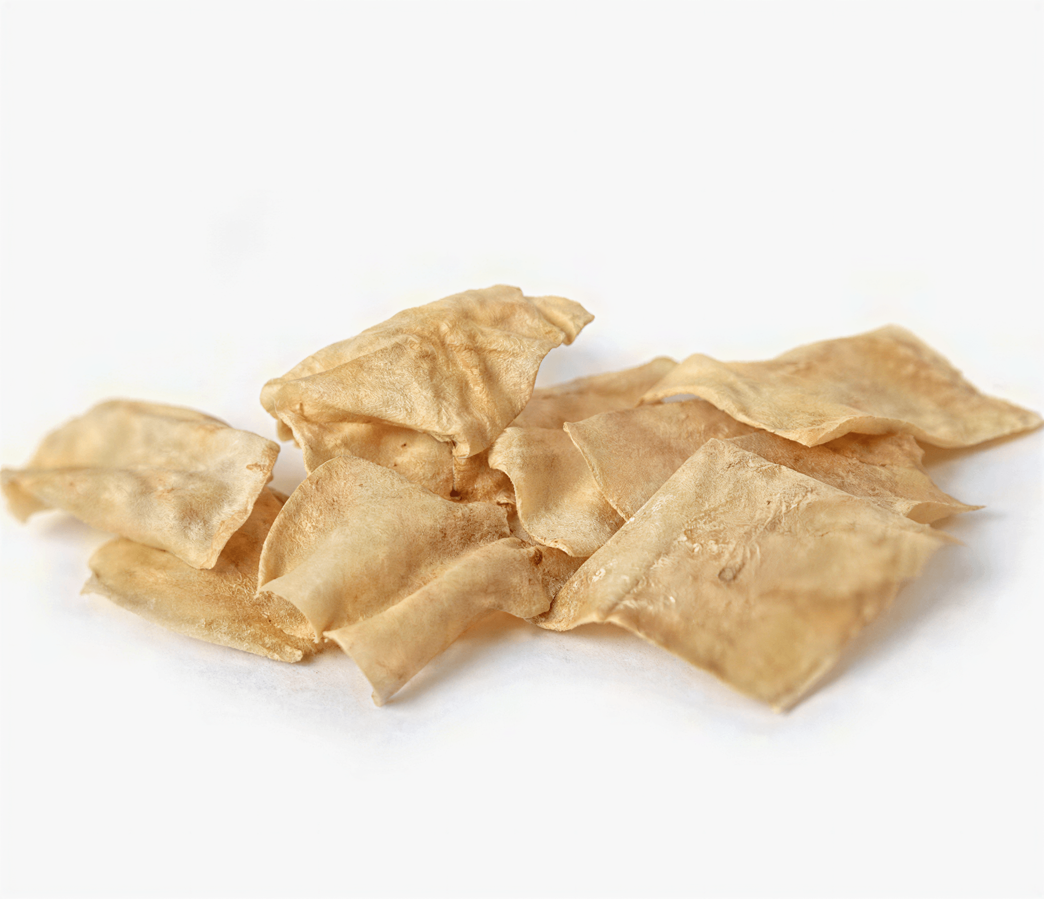 A pile of thin, rectangular tan beef collagen dog chew chips scattered on a white background.