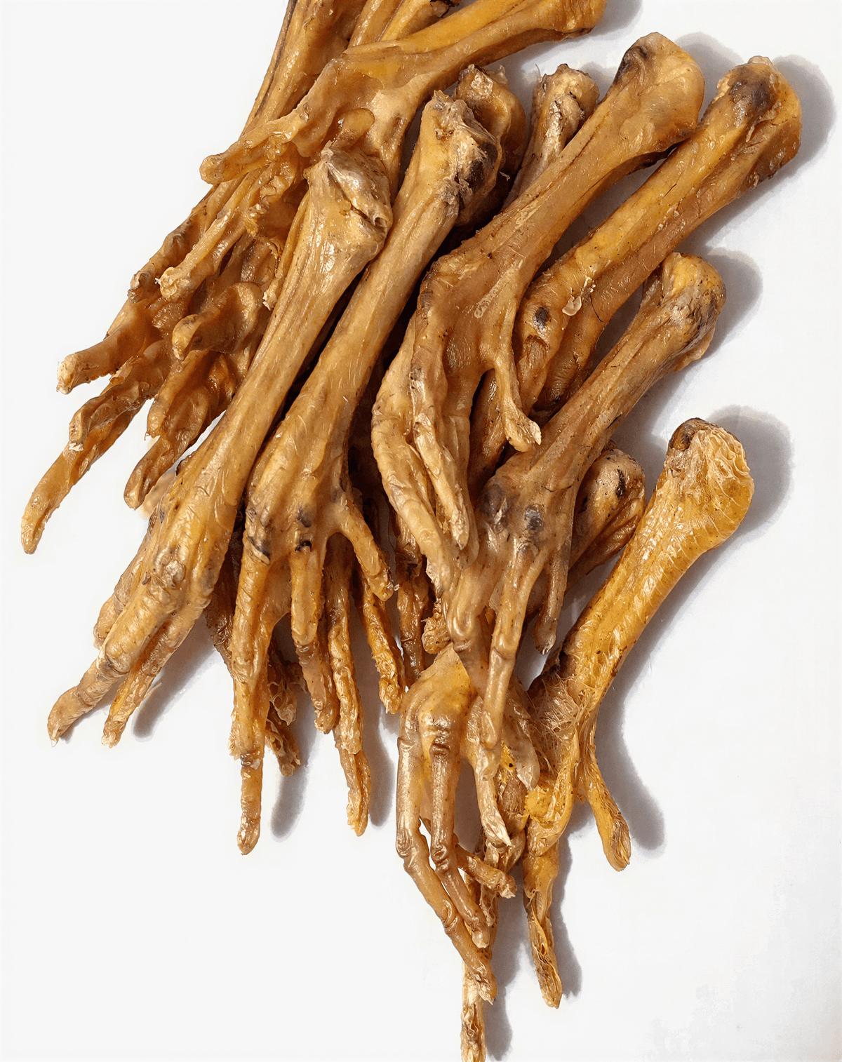 A pile of ten dried, golden-brown chicken feet dog chews arranged vertically on a white background.