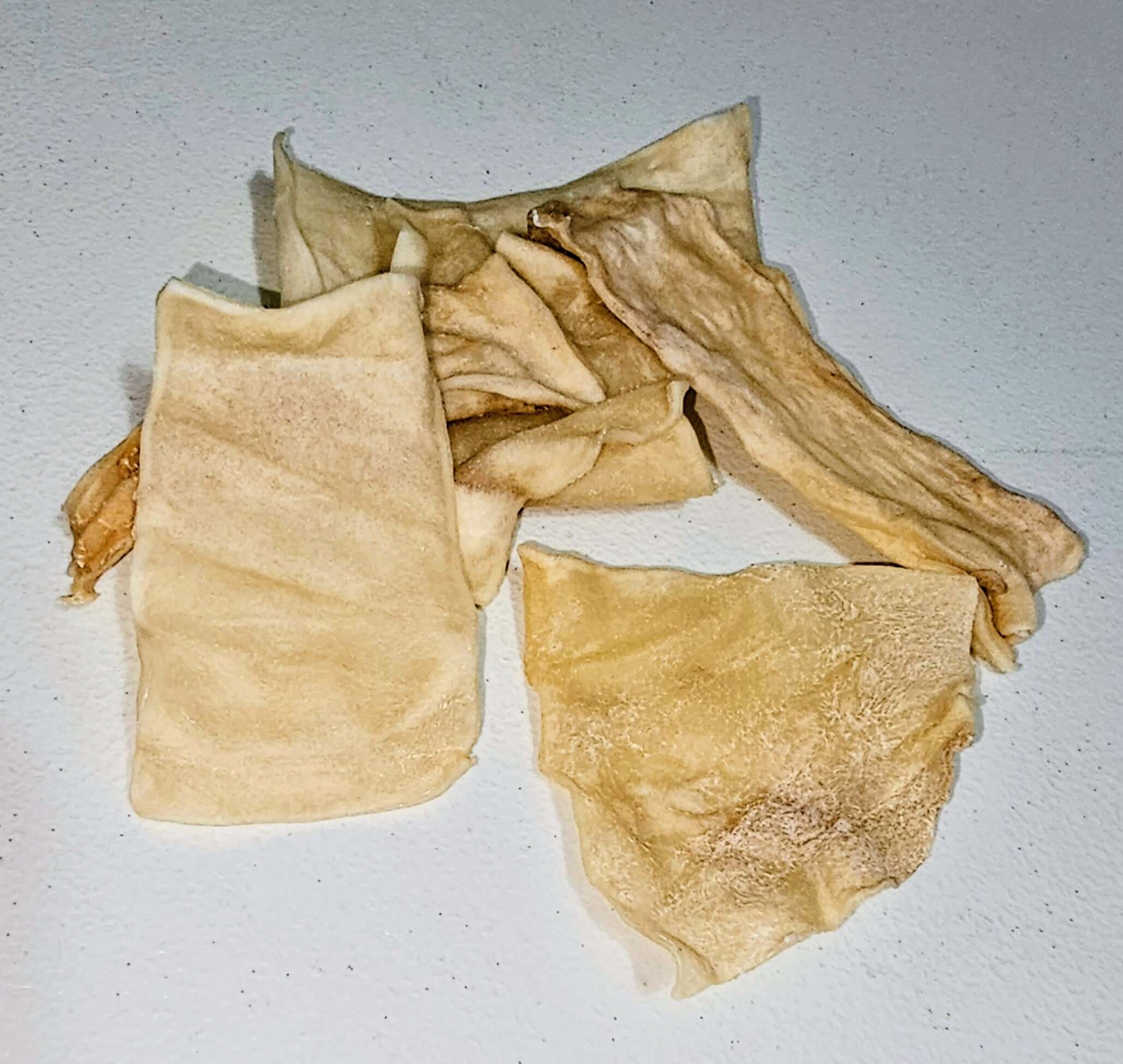 Beef collagen chips in various shapes, featuring a light beige color and a crunchy texture, arranged on a white surface.
