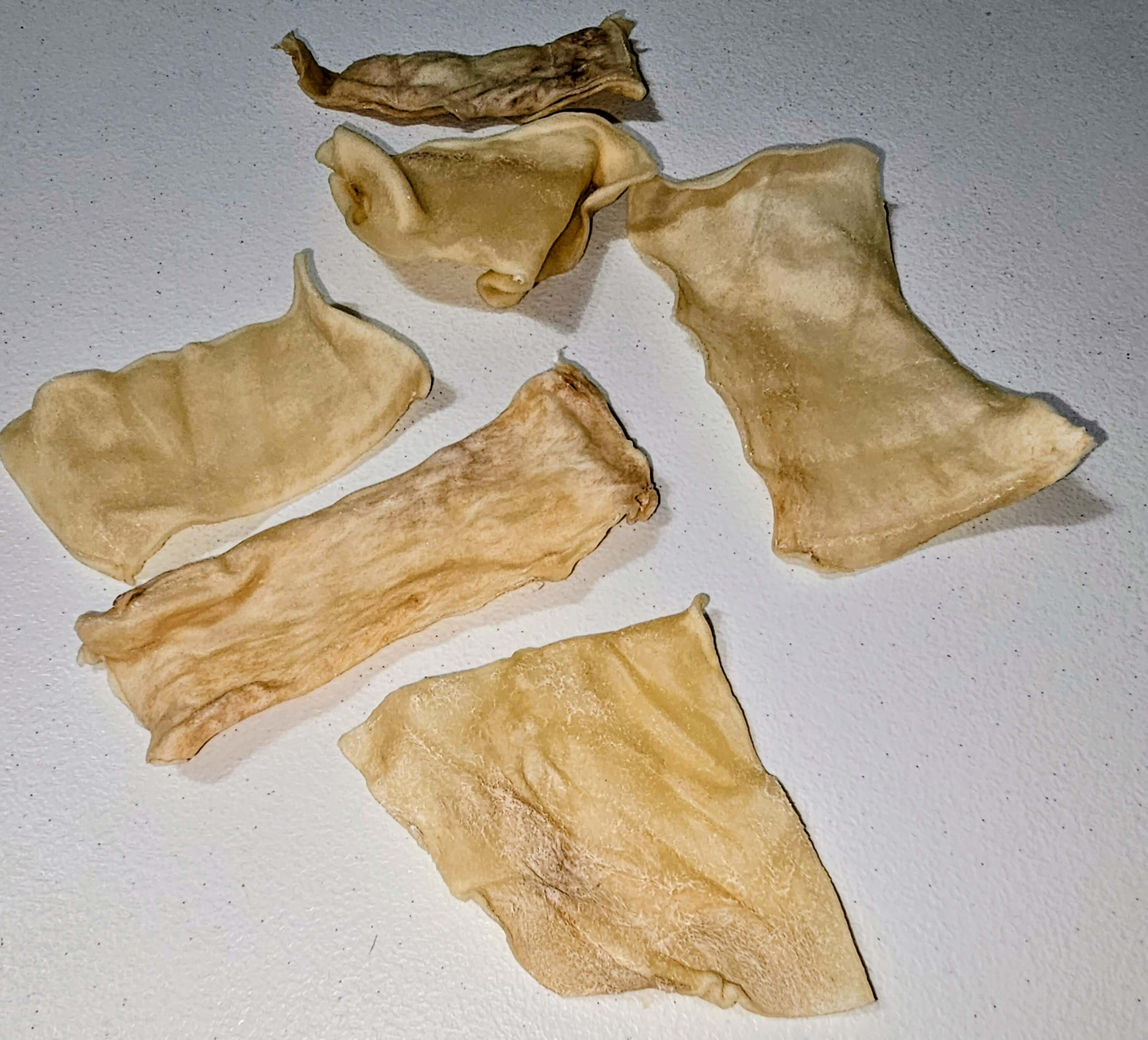 Beef collagen chips in various shapes, light tan color, arranged on a white surface, suitable for dog chews.