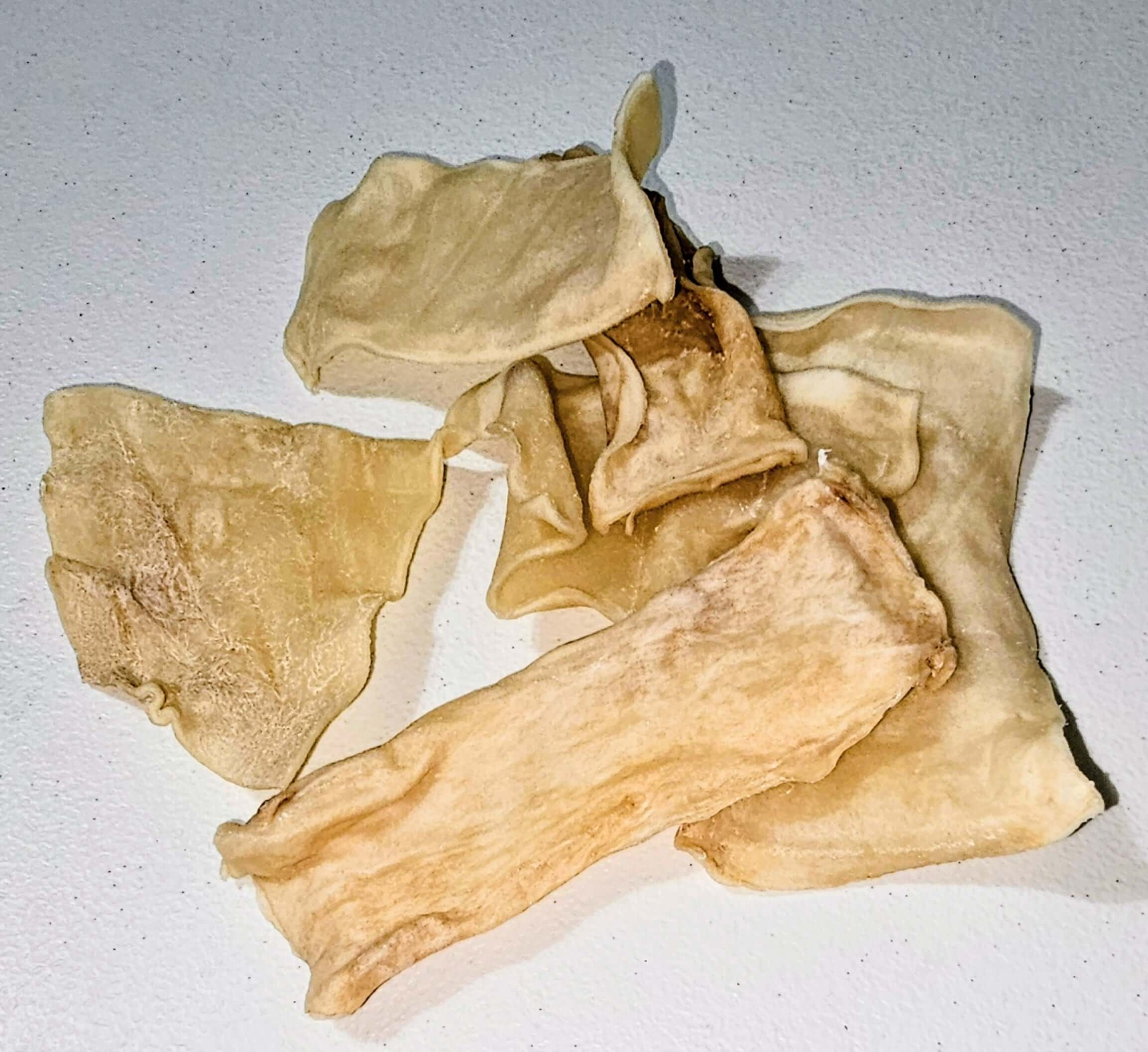 Beef collagen chips dog chews in various shapes, light beige color, arranged on a white surface.